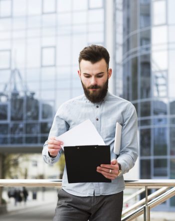 portrait-young-businessman-checking-document-front-office-building